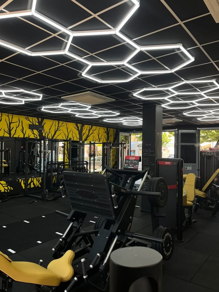 Vista d'insieme di NM Élite Studio con leg press, murale giallo e plafoniera esagonale